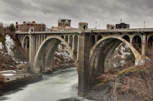A stone bridge with arches spans a river, surrounded by a cloudy sky and winter scenery.