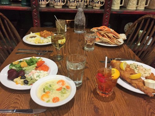 A table set with various dishes, including seafood, salad, and drinks, in a cozy dining setting.