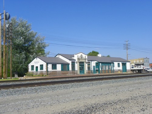Historic building with green accents, situated near railroad tracks under a clear blue sky.
