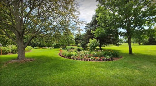 A lush green garden with colorful flower beds, surrounded by trees under a partly cloudy sky.