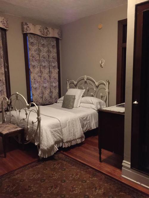 Cozy bedroom with a white bed, floral curtains, a wooden nightstand, and a patterned rug on the floor.