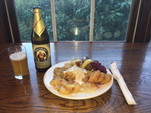 A plate of fried chicken, potatoes, red cabbage, and apples, with a beer and a glass of light beer on a wooden table.