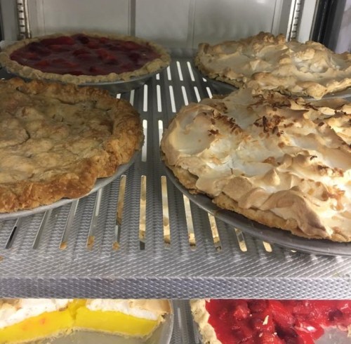 A display of various pies, including fruit and meringue-topped varieties, in a refrigerated case.