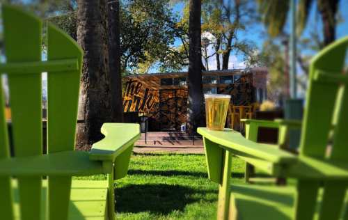 A sunny outdoor scene with green chairs, a glass of beer, and a colorful mural in the background.