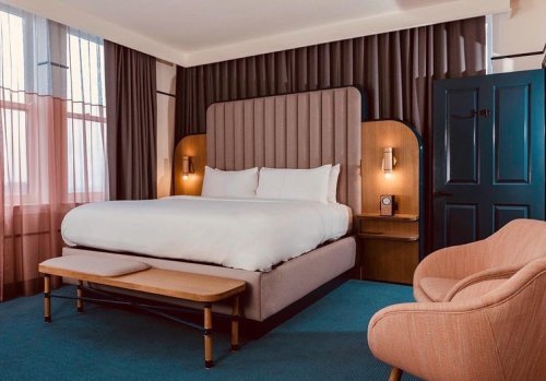 A stylish hotel room featuring a large bed, cozy armchair, and elegant decor with soft lighting and curtains.