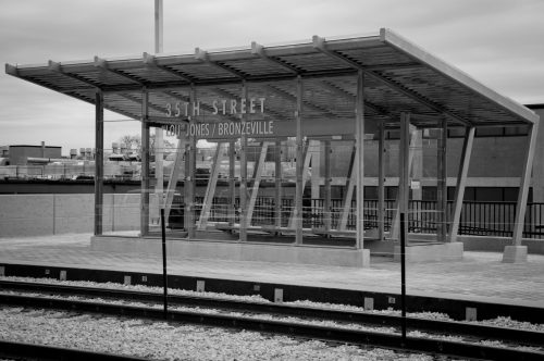 A modern train station shelter at 35th Street, featuring a glass and metal design, with tracks visible in the foreground.