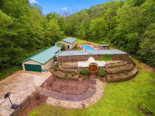 Aerial view of a unique home with stone landscaping, surrounded by lush greenery and a pool in the background.