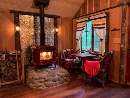 Cozy cabin interior with a stone fireplace, wooden walls, and a table by a window, adorned with a red blanket.