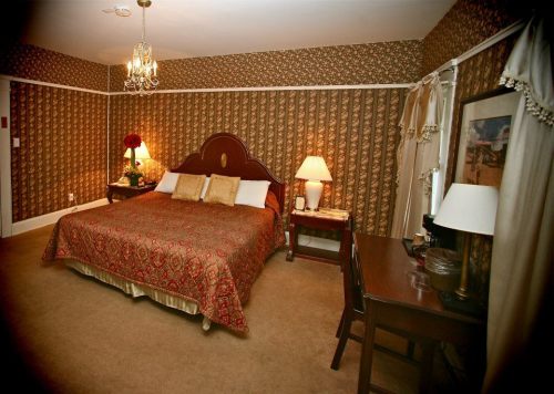 Cozy bedroom with a patterned bedspread, bedside lamps, a small table, and elegant wallpaper.