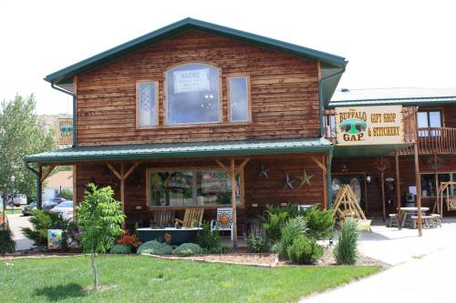 A rustic wooden building with a green roof, featuring a gift shop and signage for "Buffalo Gap." Lush landscaping surrounds it.