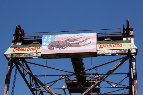 Sign on a bridge tower featuring a lobster and the text "Breaux Bridge, Louisiana" against a blue sky.