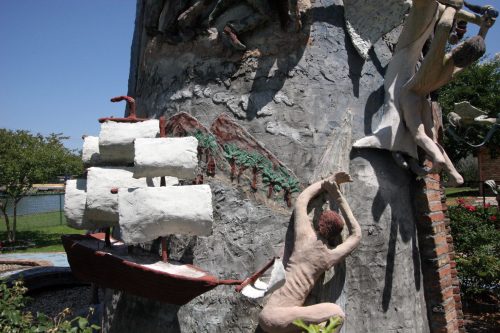 Sculptural artwork featuring a ship, human figures, and natural elements on a textured wall.