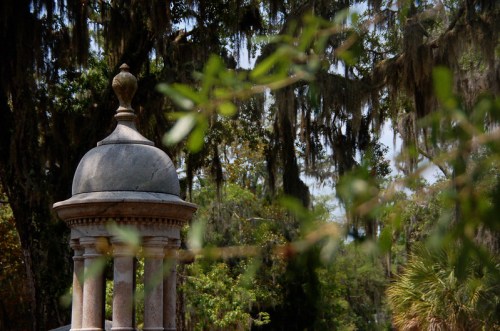 A stone structure with a dome surrounded by lush greenery and hanging moss in a serene outdoor setting.