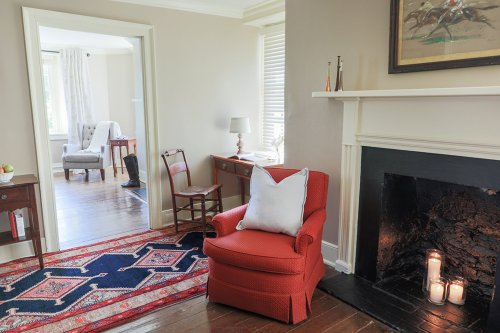 Cozy living room with a red chair, fireplace, and a view of an adjacent room with a desk and chair.