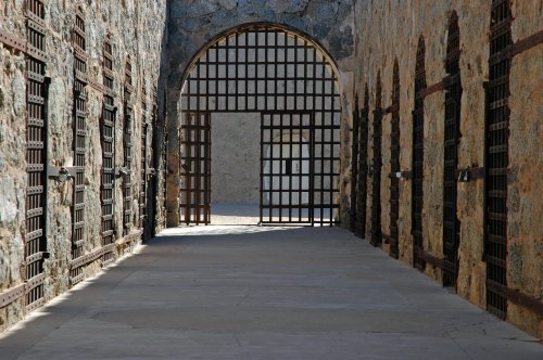 A stone corridor with barred doors on either side, leading to an open archway at the end.