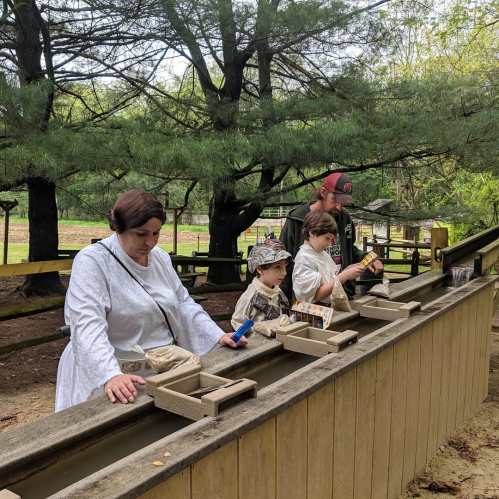 A family enjoys a gem mining activity, sifting through a water trough with tools in a natural setting.