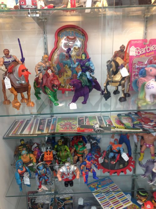 A display case filled with various vintage action figures, toys, and collectibles, including superheroes and dolls.