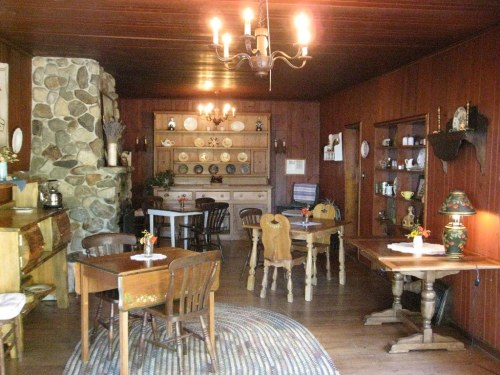 Cozy dining room with wooden furniture, a stone fireplace, and decorative plates on the walls. Warm, inviting atmosphere.