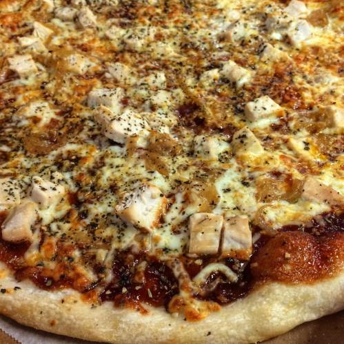 A close-up of a pizza topped with cheese, diced chicken, and herbs on a golden crust.