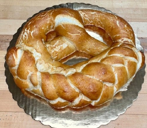 A large, golden-brown braided pretzel on a round silver platter.