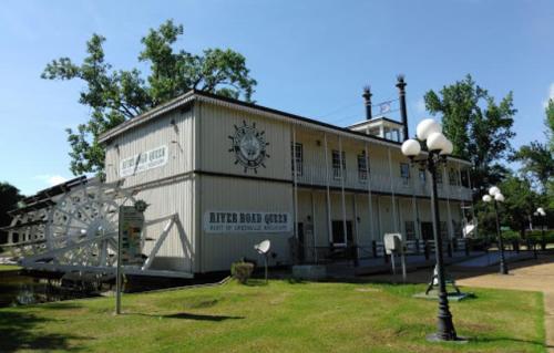 A riverboat-themed building with a paddlewheel, surrounded by green grass and trees under a clear blue sky.