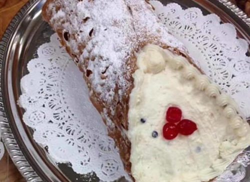 A decorated yule log cake on a silver platter, dusted with powdered sugar and topped with red cherries.