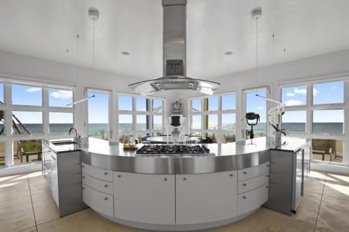 Modern kitchen with a curved island, stainless steel appliances, and large windows overlooking the ocean. Bright and airy space.