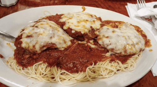 A plate of spaghetti topped with marinara sauce and three cheese-covered meatballs.