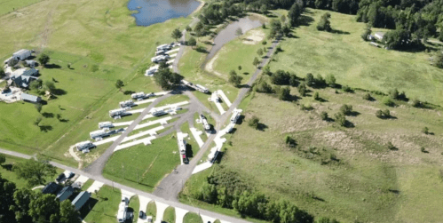 Aerial view of a campground with RVs parked along winding paths, surrounded by green fields and a small pond.