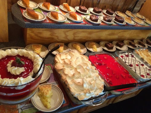 A variety of desserts displayed on plates, including cakes, pies, and a large trifle with whipped cream and fruit.
