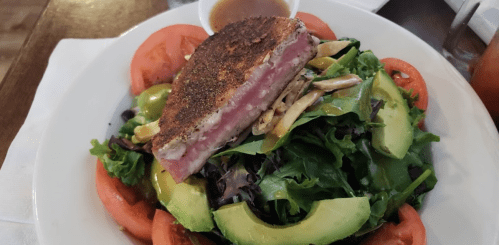 A vibrant salad topped with seared tuna, avocado, tomatoes, and a drizzle of dressing on a bed of mixed greens.