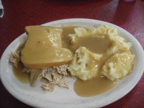 A plate of shredded chicken topped with gravy, served alongside creamy mashed potatoes and additional gravy.