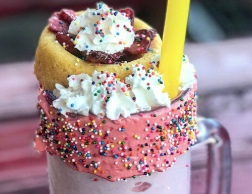 A colorful milkshake topped with whipped cream, sprinkles, and a cookie filled with strawberries.