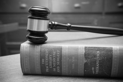 A gavel rests on an old medical book titled "The Practitioners' Library of Medicine and Surgery, Vol. VIII."