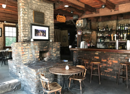 Cozy restaurant interior featuring a brick fireplace, wooden bar, and tables in a warm, inviting atmosphere.