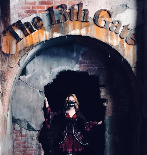 A woman in a red dress and mask stands in a crumbling archway labeled "The 13th Gate."