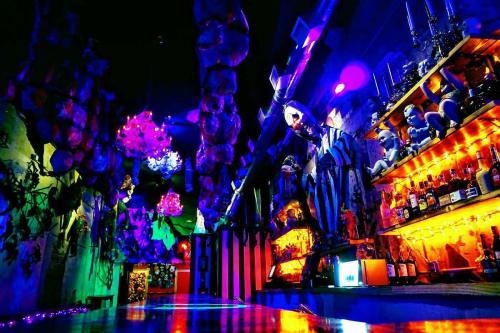 A vibrant, eclectic bar interior with colorful lighting, unique decor, and shelves filled with bottles.