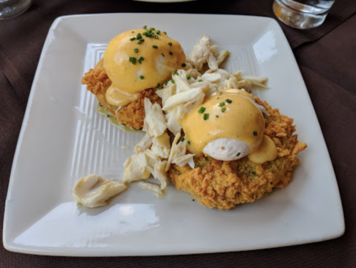 Two crab cakes topped with poached eggs and hollandaise sauce, garnished with chives, served on a white plate.