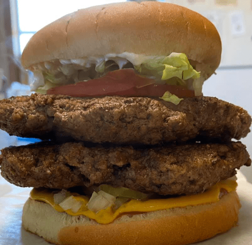 A towering burger with two beef patties, cheese, lettuce, tomato, and mayonnaise on a soft bun.