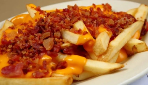 A plate of crispy fries topped with melted cheese and crumbled bacon.