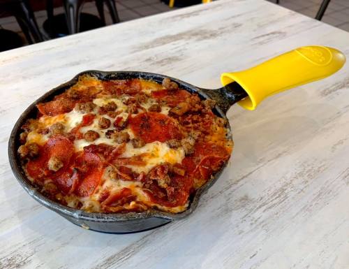 A skillet filled with cheesy baked pasta topped with pepperoni and sausage, resting on a white table.