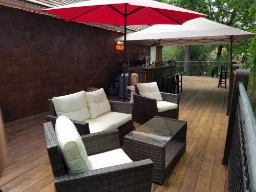 Cozy outdoor seating area with wicker furniture, white cushions, and red umbrellas on a wooden deck.