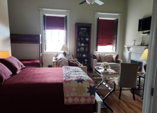 Cozy bedroom with a quilted bed, seating area, and natural light from windows, featuring warm decor and a TV.