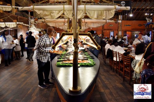 A buffet setup on a boat-shaped table with diners serving seafood in a nautical-themed restaurant.