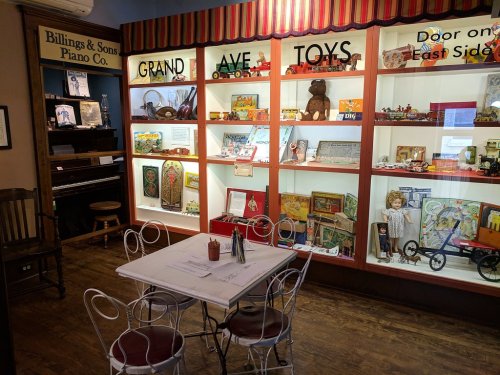 A cozy room with a display of vintage toys and a small table with chairs, featuring a piano in the background.