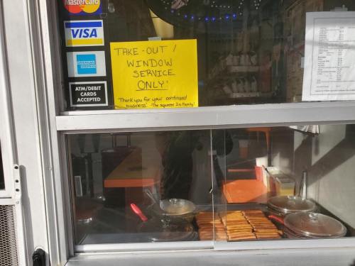 Take-out window service sign at a food stall, with visible cooking equipment and a payment options display.