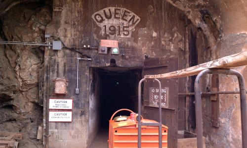 Entrance to a mine tunnel marked "QUEEN 1915," with a trolley signal and caution signs visible.