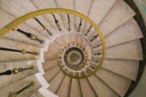 Aerial view of a spiral staircase with stone steps and a brass railing, creating a mesmerizing pattern.