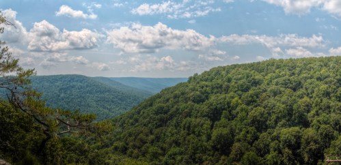 A panoramic view of lush green hills under a partly cloudy sky, showcasing a serene natural landscape.