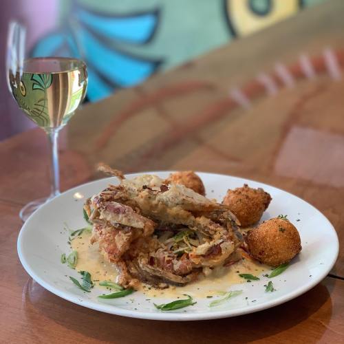 A plate of crispy fried food with a creamy sauce, accompanied by two golden croquettes and a glass of white wine.